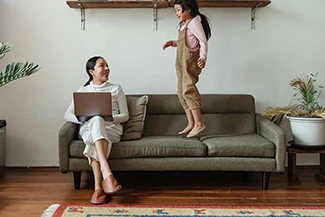 A woman and child sit together on a couch, using a laptop, exemplifying the balance of work and family life.